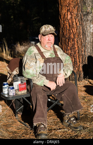 Un homme âgé habillé en salopette est assis sur une chaise près du camp Metolius, Oregon Banque D'Images
