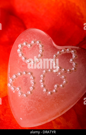 Formes coeur incorporé dans un coeur de glace artificielle sur des pétales de rose Banque D'Images