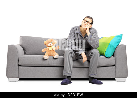 Jeune homme en pyjama dans les pensées profondes assis sur un canapé avec un ours en peluche à côté de lui Banque D'Images