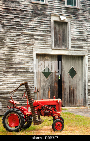 Un ancien International rouge bas tracteur Cub garçon assis en face d'une vieille grange en bois. Banque D'Images