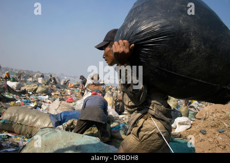 Un homme qui est une chasse travailleur est l'accomplissement d'un grand sac rempli de déchets à la décharge de Stung Meanchey à Phnom Penh, Cambo Banque D'Images