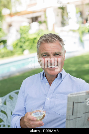 Senior man reading newspaper and drinking wine in backyard Banque D'Images