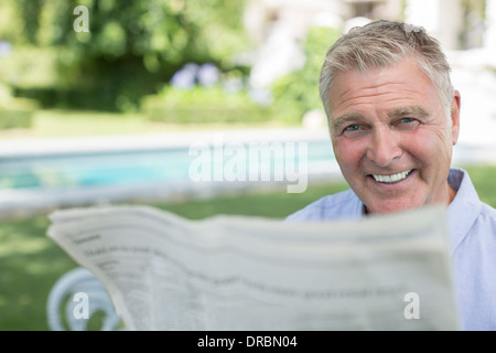 Senior man reading newspaper at poolside Banque D'Images