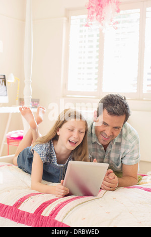 Père et fille using digital tablet on bed Banque D'Images