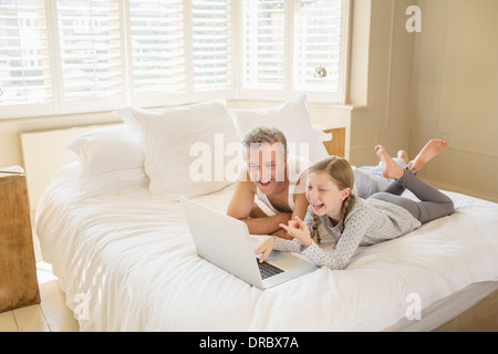 Père et fille using laptop on bed Banque D'Images