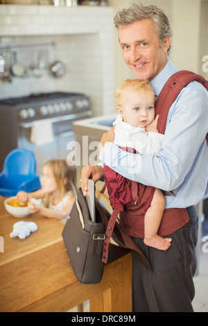 Businessman carrying baby in kitchen Banque D'Images