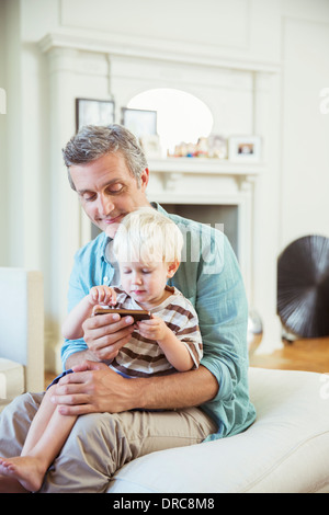 Père et fils using cell phone in living room Banque D'Images