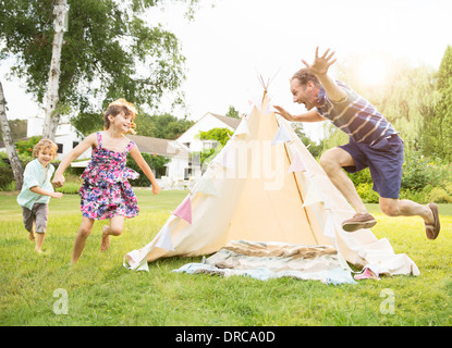 Père chassant les enfants autour de tipi in backyard Banque D'Images