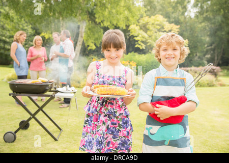 Frère et sœur maintenant près de maïs grillés au barbecue jardin Banque D'Images