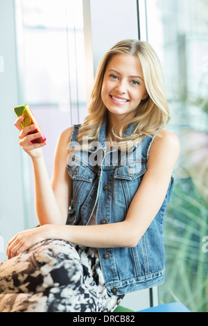 Woman using cell phone by window Banque D'Images