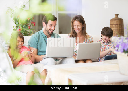 Famille avec des ordinateurs portables, tablettes numériques et de téléphones cellulaires sur canapé patio Banque D'Images