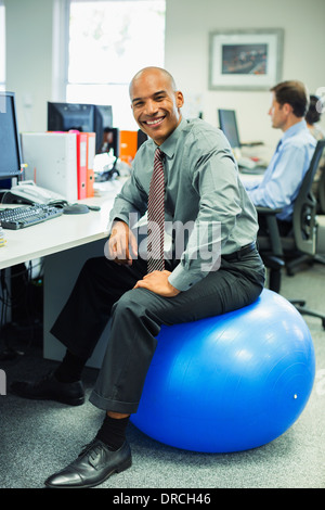 Businessman sitting on fitness ball in office Banque D'Images