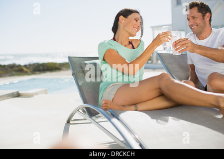 Couple toasting verres à eau dans des chaises longues au bord de la piscine Banque D'Images