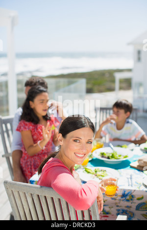 Family eating lunch at table sur un patio ensoleillé surplombant Ocean Banque D'Images