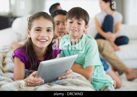 Enfants using digital tablet on sofa in living room Banque D'Images