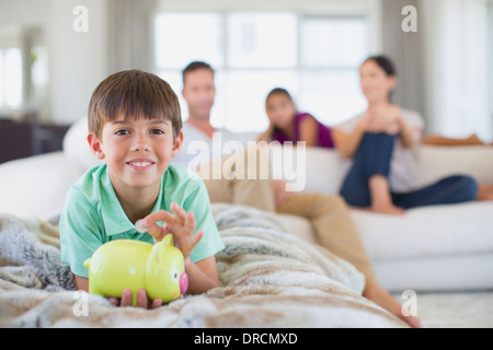 Boy with piggy bank on sofa in living room Banque D'Images