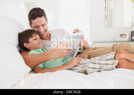 Père et fils using digital tablet on bed Banque D'Images