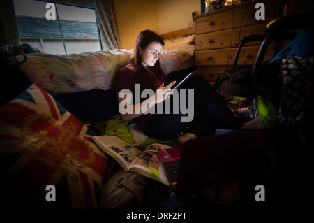 Une jeune femme étudiant de l'université travaillant sur un iPad dans sa chambre en désordre à la maison UK dans sa chambre à coucher à la maison UK Banque D'Images