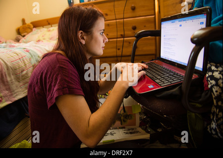 Une jeune femme étudiant de l'université travaillant sur son ordinateur portable dans sa chambre en désordre à la maison UK Banque D'Images