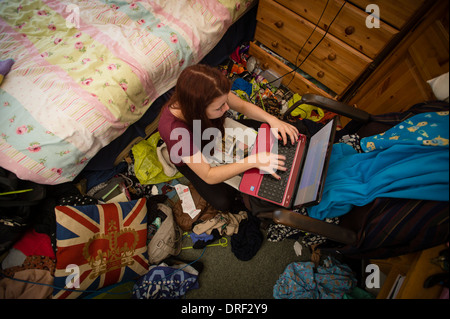 Une jeune femme étudiant de l'université travaillant sur son ordinateur portable dans sa chambre en désordre à la maison UK Banque D'Images