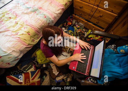 Une jeune femme étudiant de l'université travaillant sur son ordinateur portable dans sa chambre en désordre à la maison UK Banque D'Images