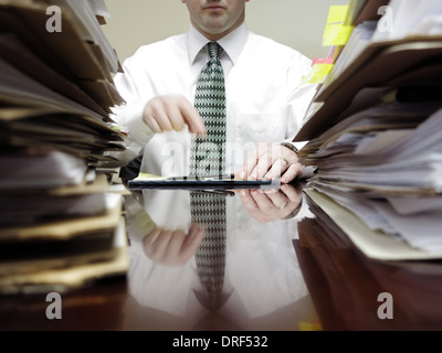 Businessman sitting at desk avec bloc de papier et des piles de dossiers Banque D'Images