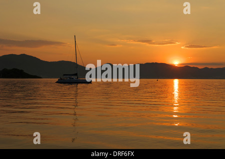 Ancré au large des côtes en catamaran au coucher du soleil Banque D'Images