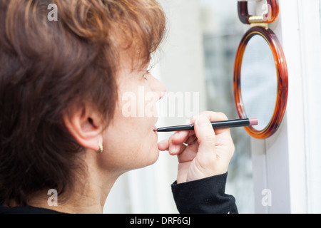 Femme d'âge moyen et à l'application d'un crayon à lèvres dans le miroir. Banque D'Images