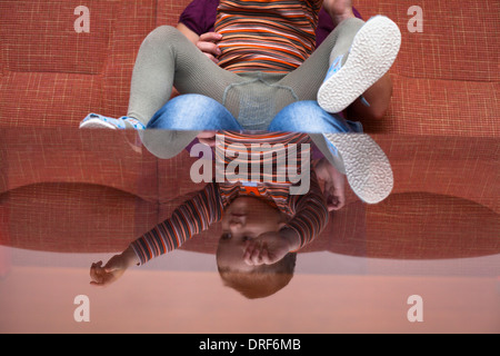 Garçon enfant ludique reflète dans une table en verre sitting on sofa at home Banque D'Images