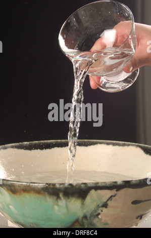 On verse de l'eau dans un verre dans un bol. Banque D'Images