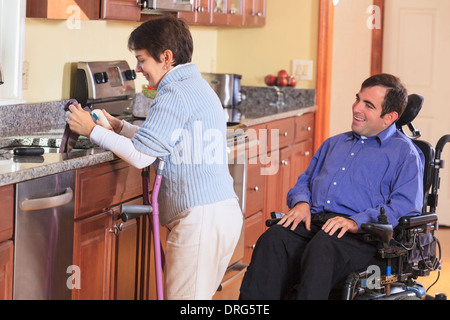 Femme avec la paralysie cérébrale à l'aide de béquilles et travaillant dans sa cuisine tout en parlant à son mari avec la paralysie cérébrale Banque D'Images