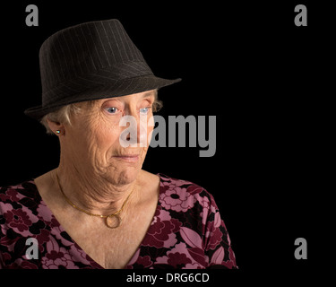 Senior lady avec un air choqué sur son visage portant un fedora isolated on black Banque D'Images