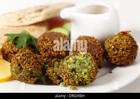 Des falafels (salade de pois chiches épicés et balles) sur une plaque avec le pain plat égyptien, les tranches de citron, de la salade et une sauce tahina. Banque D'Images