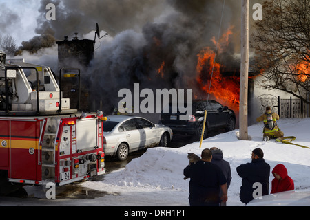 En hiver à l'extérieur de la famille regarde pendant que house va en flammes avec des pompiers de pulvériser de l'eau pour abattre le blazing fire structurels Ottawa Banque D'Images