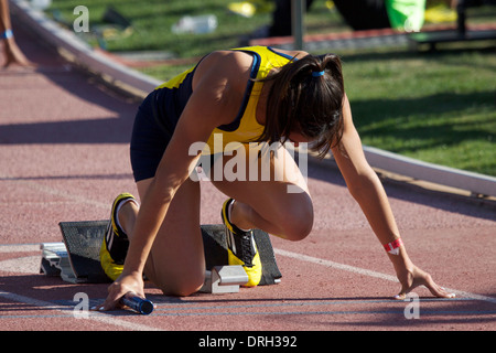 Athlète féminin dans les starting-blocks à un track and field rencontrez un jour ensoleillé chaud en Californie USA Banque D'Images