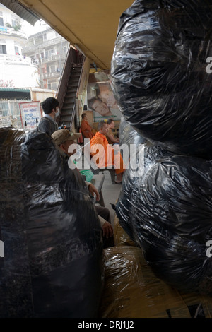 Un moine bouddhiste est en attente d'un bus près de grands sacs en plastique remplis de marchandises au Sorya dépôt de bus de Phnom Penh, Cambodge. Banque D'Images