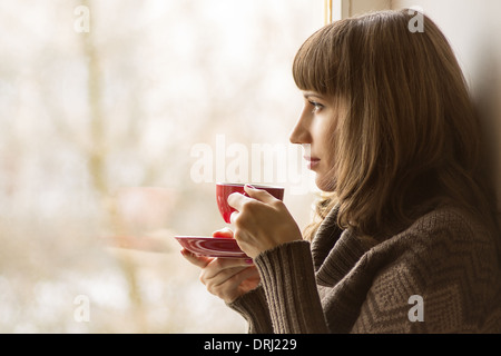 Belle fille de boire du café ou thé fenêtre proche Banque D'Images