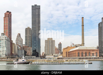 Un remorqueur poussant une barge sur l'East River et de Manhattan est à l'arrière-plan. Banque D'Images