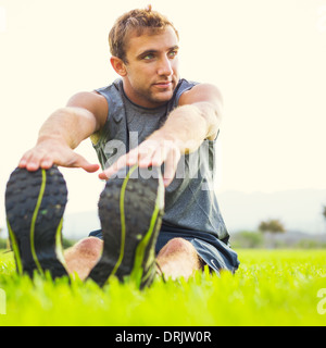 Jeune homme fit attrayants les étirements avant l'exercice, le lever du soleil tôt le matin et rétroéclairées. Vie saine remise en forme sport concept. Banque D'Images