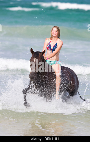 Cheval Kaimanawa. Jeune femme riant sur hongre alezan trotting en surf, sans selle et tactique. Nouvelle Zélande Banque D'Images