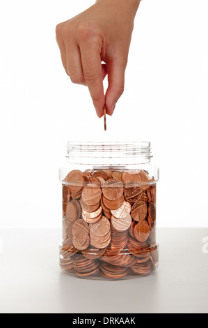 Jeune femme part de placer une pièce dans un pot d'épargne. Banque D'Images