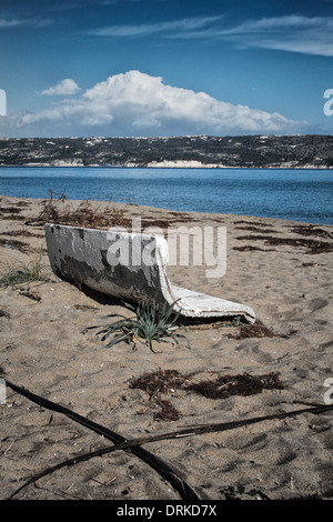 Une plage en hiver avec un banc de béton à demi submergée dans le sable. Une baie de mer bleue, une péninsule et ciel bleu avec des nuages blancs. Banque D'Images