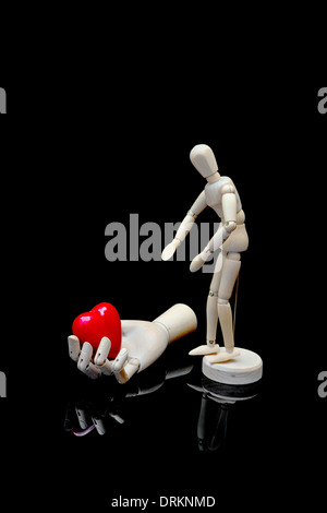 Un mannequin de bois et une main en bois avec cœur rouge sur fond noir Banque D'Images