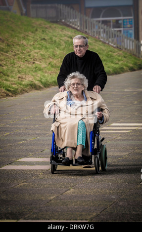 Homme poussant une femme âgée en fauteuil roulant le long du front de mer à Whitley Bay, North Tyneside. Banque D'Images