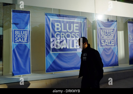 Homme marchant passé Blue Cross Vente posters at DEBENHAMS department store à Luton Banque D'Images