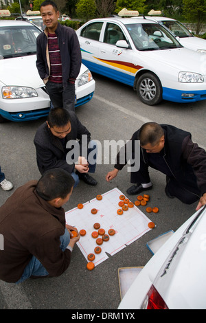 Les chauffeurs de taxi chinois attendent les passagers / les chauffeurs de taxi s'occupent d'eux-mêmes en jouant / en jouant à un jeu de plateau d'échecs chinois Xiangqi dans la rue avec leurs voitures de taxi.Chine Banque D'Images