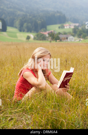 L'Autriche, Salzkammergut, Mondsee, young woman reading book in a meadow Banque D'Images