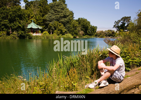 Jeune garçon assis à côté de Lac Stow, Golden Gate Park, San Francisco, CA, California, USA Banque D'Images