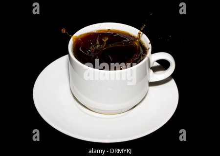 Cube de sucre est tombé dans une tasse de café isolé sur un fond noir Banque D'Images