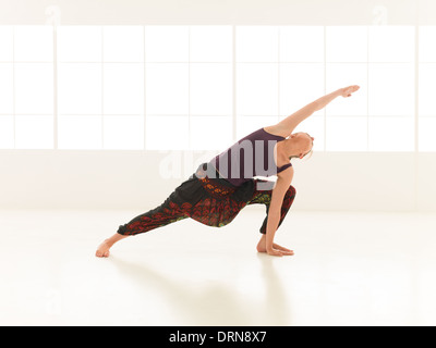 Jeune femme démontrant la posture de yoga avancée, dans une salle vide avec lumière naturelle. Banque D'Images